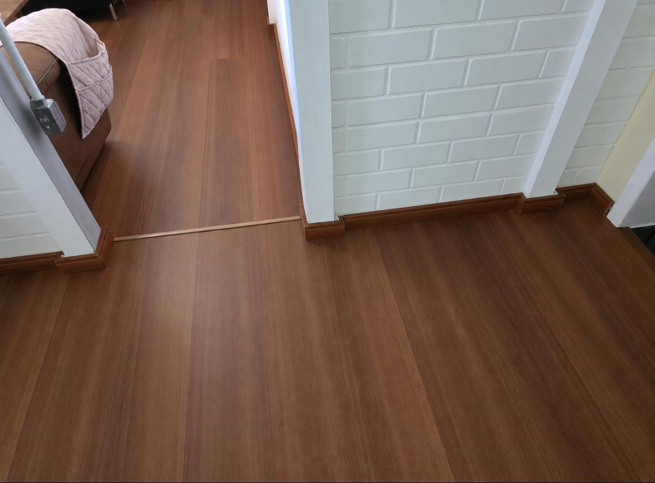 Sala com piso laminado amadeirado escuro e rodapé em tom mel